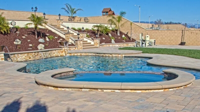 Curved pool situated outdoors with a spa and lush vegetation. Photo