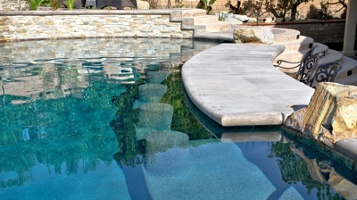 Arid refuge adorned with a pool and spa, framed by rugged rocks and verdant palms. Photo