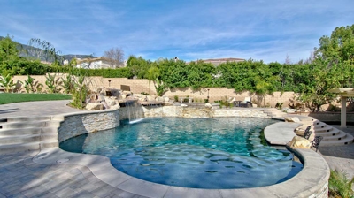 Oasis showcasing a pool and spa amidst rugged rocks and lush palms. Photo