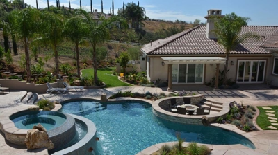 Verdant backyard oasis featuring a pool, spa, and built-in fire pit. Photo