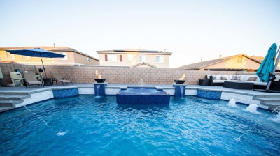 Expansive backyard featuring a blue-tiled swimming pool, complete with a spa and captivating fire elements. Photo