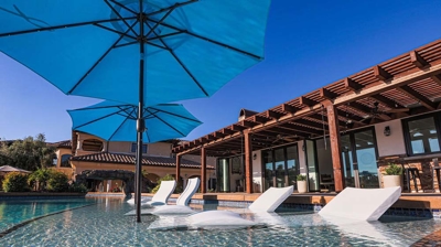 Desert-style pool haven featuring submerged seating and umbrella-shaded loungers. Photo