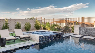 Modern pool surrounded by landscaping, lawn chairs, and hot tub. Photo