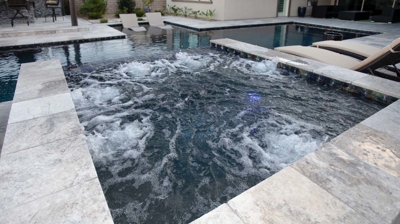 Bubbling hot tub that flows into pool with lounging area in the shallow end. Photo