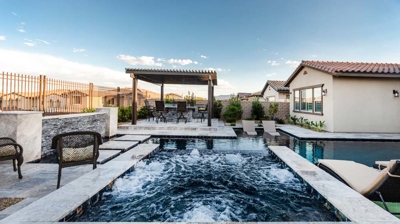 Luxurious backyard pool area with bubbling hot tub and shaded outdoor kitchen. Photo