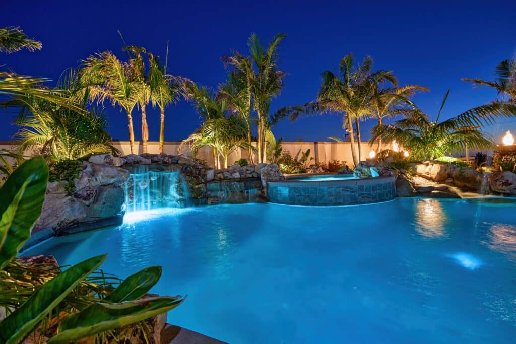 Pool with lights and a fountain with tropical landscaping