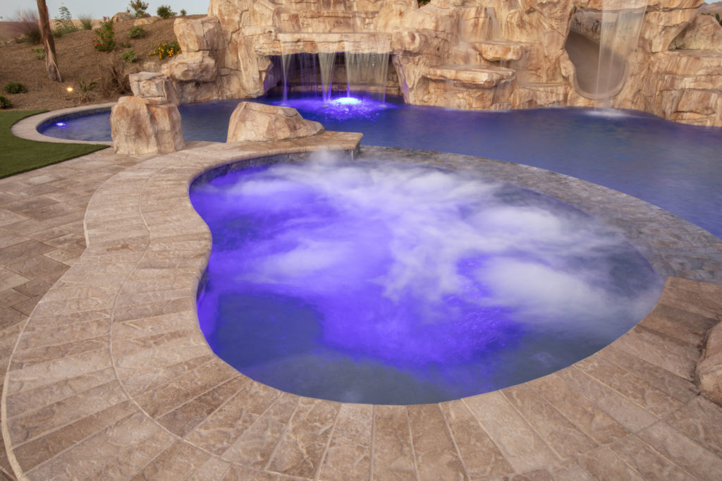 A beautiful pool with jacuzzi and blue lighting and some fountain with a slide