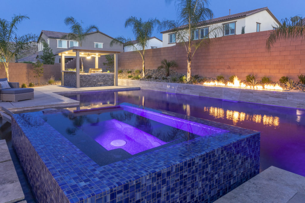A pool with purple light accent and a floating fire pit